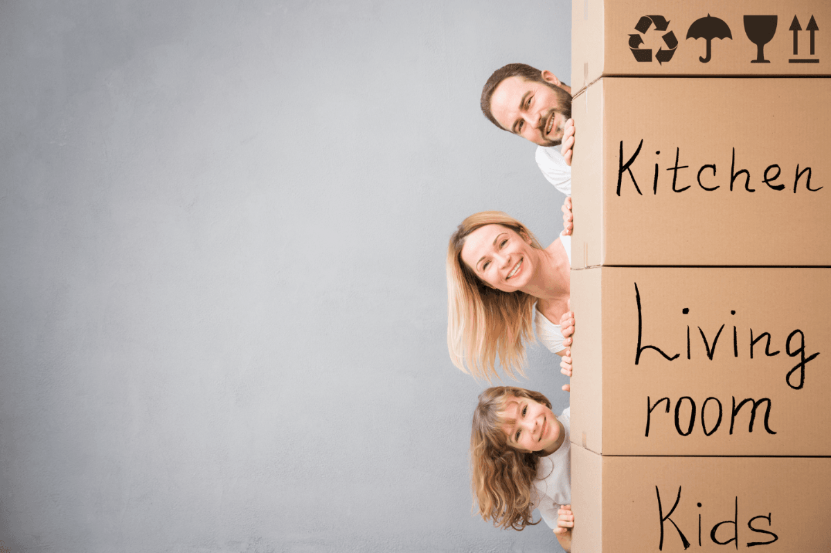 A family peeking around a stack of labeled moving boxes
